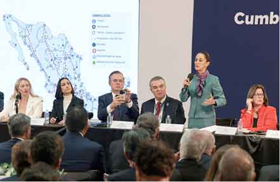 Un grupo de personas se sienta en una mesa larga durante una conferencia. Una mujer habla por un micrófono mientras está de pie. En una pantalla de fondo se muestra un mapa de México.