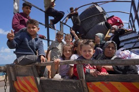 Niños y adultos en un camión, algunos sentados, otros de pie, bajo un cielo despejado.