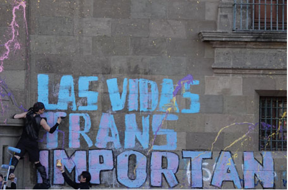 Un hombre está pintando un mural en el costado de un edificio con las palabras las vidas trans importante.