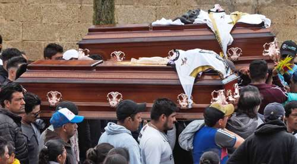 Una multitud de personas se reÃºne alrededor de dos ataÃºdes de madera adornados con prendas y adornos durante un cortejo fÃºnebre.