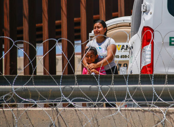 Una mujer y un niño están junto a una valla de alambre de púas.