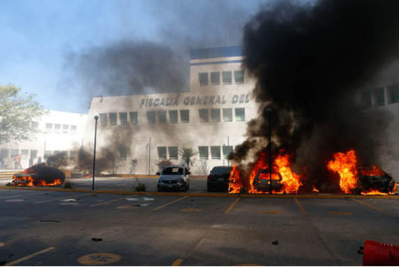 Vehículos incendiados frente a un edificio con el letrero "fiscalía general de la república".