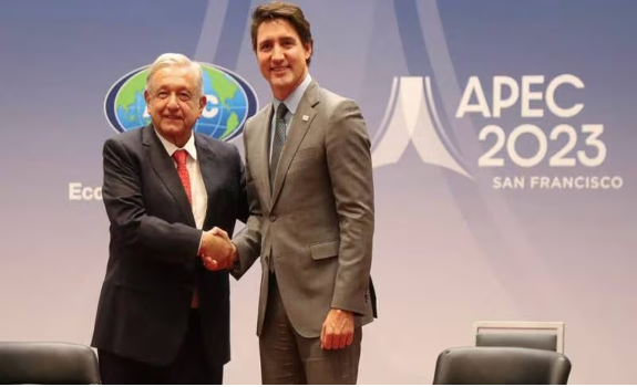 Dos hombres se dan la mano frente a un cartel de APEC.