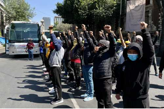 Un grupo de personas con los puños en alto frente a un autobús.