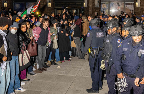 Manifestantes frente a una fila de agentes del Departamento de PolicÃ­a de Nueva York durante una manifestaciÃ³n nocturna.