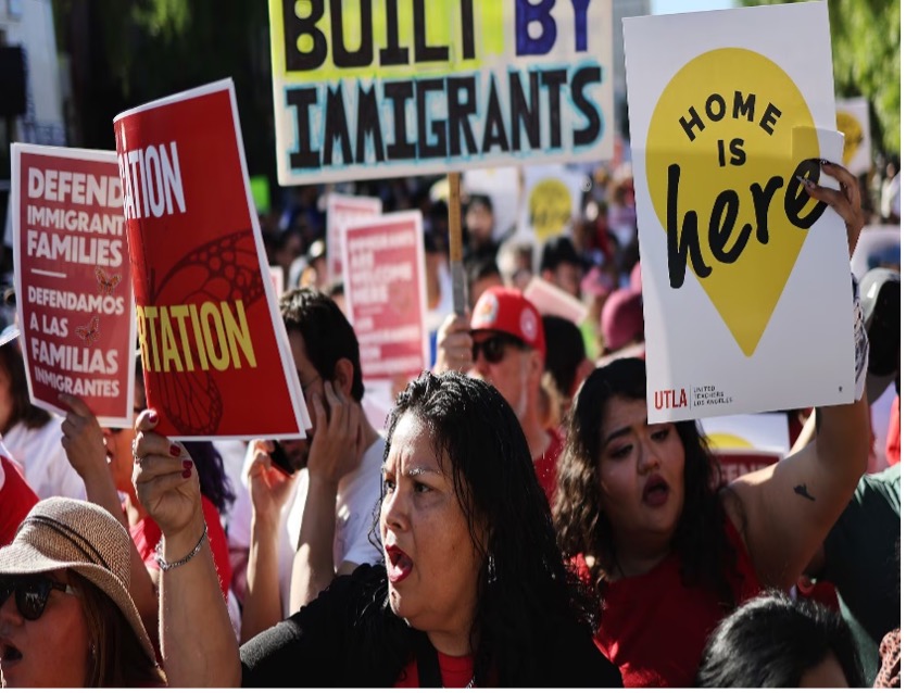 Un grupo de manifestantes sostiene carteles relacionados con la inmigración, incluidos "El hogar está aquí" y "Defendamos a las familias inmigrantes" durante una manifestación.