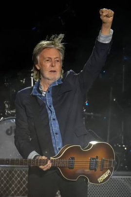 Un hombre que lleva una chaqueta estÃ¡ de pie en el escenario sosteniendo una guitarra, con un brazo levantado en un puÃ±o.