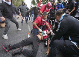 Un grupo de personas atiende a una persona herida que yace en el suelo durante una reunión pública.