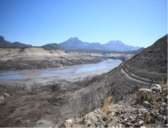 Un lecho de río seco se extiende a través de un paisaje árido con montañas distantes bajo un cielo azul claro.