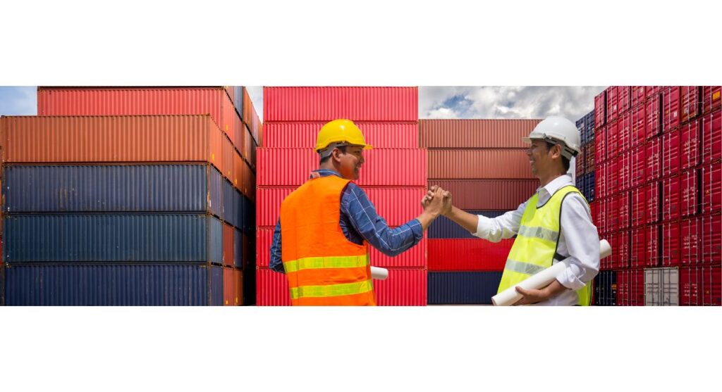 Dos trabajadores de la construcción vestidos con equipo de seguridad se dan la mano, sellando una asociación frente a contenedores de envÃo apilados, mientras se aventuran en nuevos mercados.