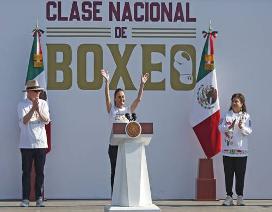 Una mujer en el podio levanta los brazos mientras dos personas a cada lado aplauden. De fondo se ve el texto "Clase Nacional de Boxeo" y dos banderas mexicanas.