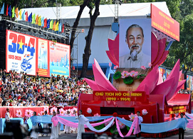 Una carroza con un retrato de Ho Chi Minh avanza ante una gran multitud, con pancartas y banderas desplegadas en el fondo.