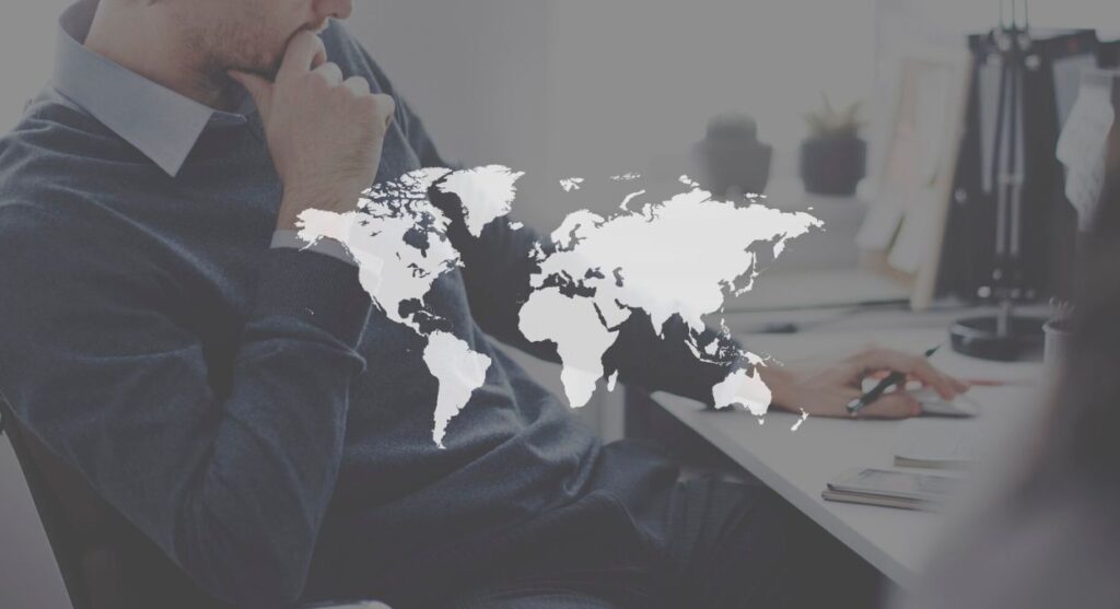 Una persona sentada en un escritorio con un bolÃ­grafo, parcialmente visible, superpuesto con un grÃ¡fico de un mapa mundial translÃºcido, que simboliza cÃ³mo las marcas se conectan a travÃ©s de las fronteras globales.