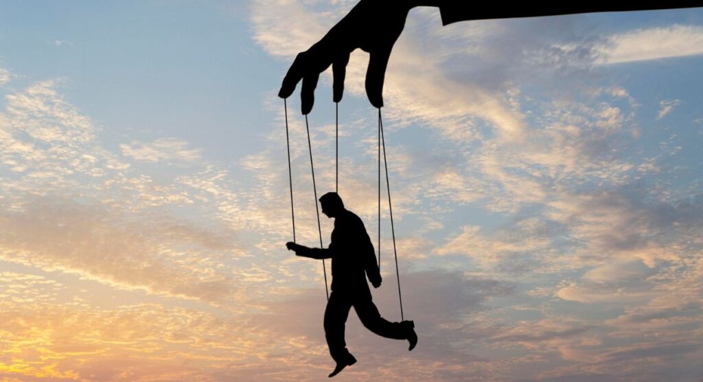 Silueta de una mano grande que controla una figura humana con cuerdas como una marioneta contra un cielo nublado al atardecer, simbolizando la resiliencia para superar el control y la adversidad.
