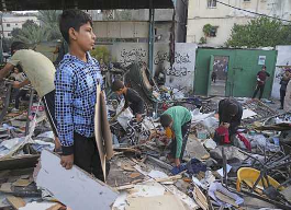 Varios niños buscan entre escombros en una zona al aire libre rodeada de muros con grafitis. Un niño en primer plano sostiene un trozo de cartón.