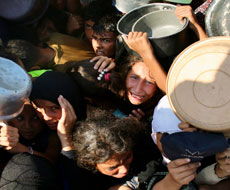 Multitud de personas con ollas y recipientes en las manos, que parecen esperar la distribución de alimentos o agua.