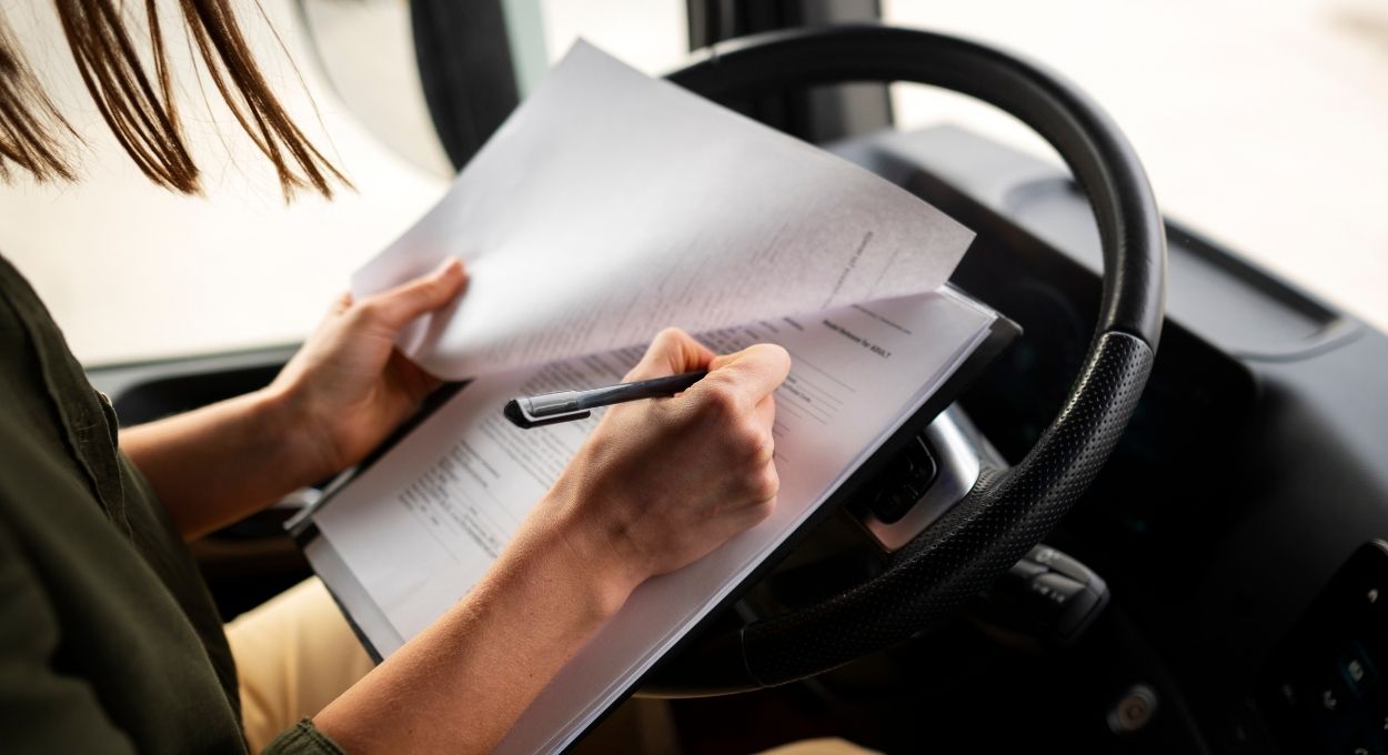 Persona sentada en un vehículo, con papeles en la mano y un bolígrafo, revisando documentos carta porte en un portapapeles apoyado en el volante.